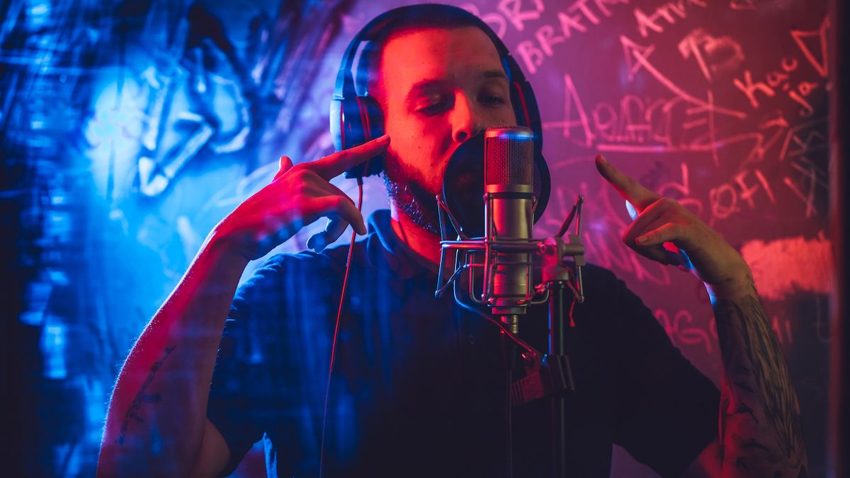 Man singing into a mic against a graffiti covered wall