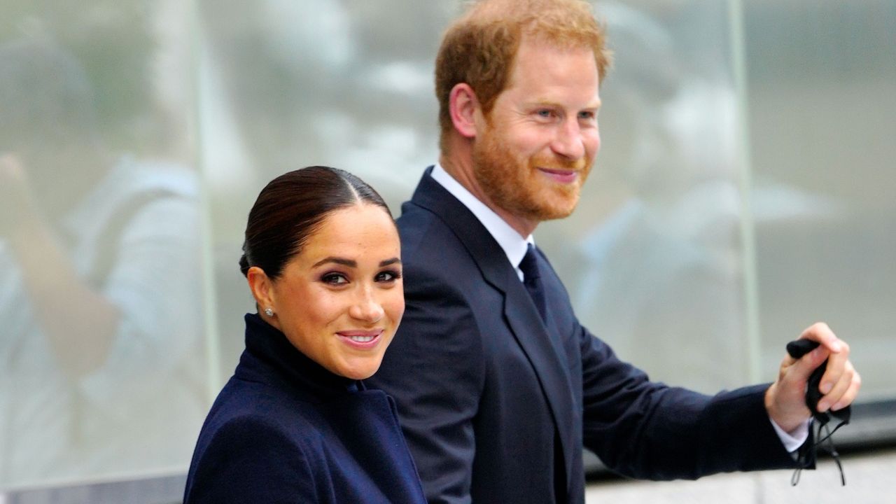 Meghan Markle smiles and waves as she walks with Prince Harry