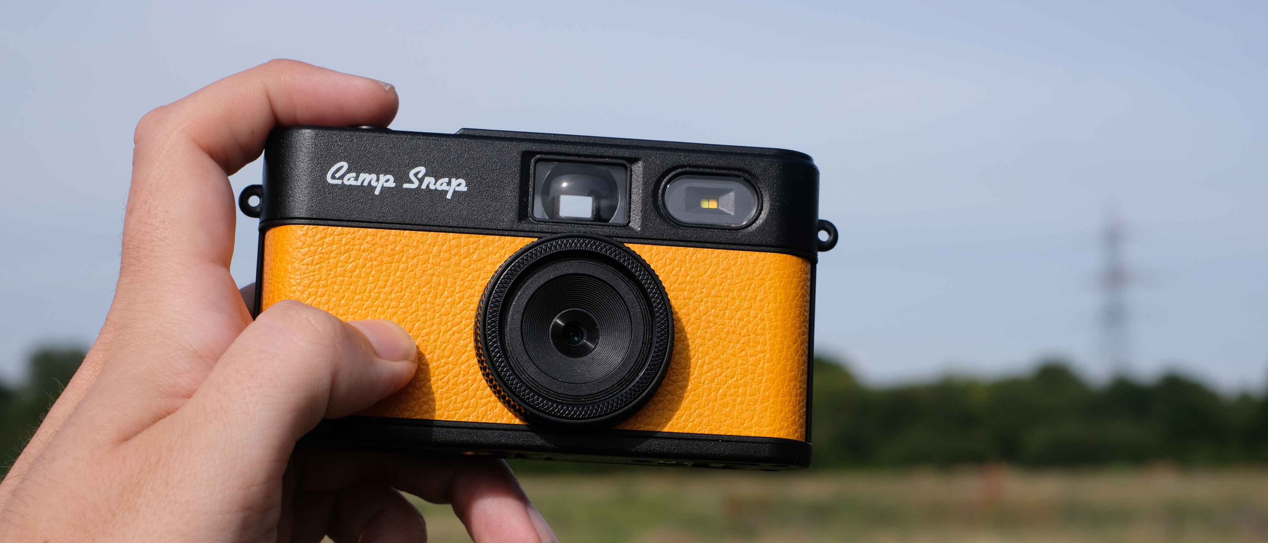 Photograph of man's hand holding Camp Snap 2 digital camera, in yellow colorway
