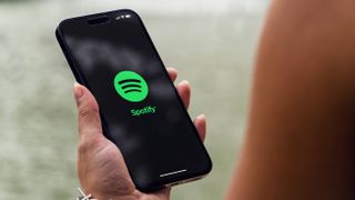 Hand holding a phone with the Spotify app logo