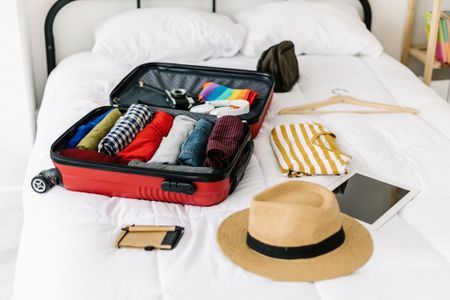 An open suitcase with a hat, device, socks, and other travel essentials