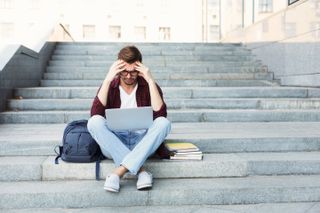 Frustrated student sitting on steps with a laptop, stock photo