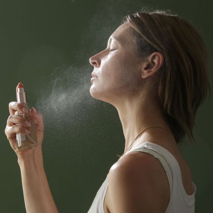 best face mists - image of a woman spraying a mist onto her face side on - gettyimages 1414252650