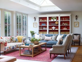 floral sofa and blue sofa with grey armchairs in room with red-paneled white display shelves roof lantern and french windows