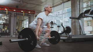 Older man performs a deadlift in the gym