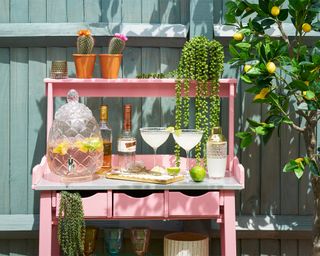 A pink painted outdoor bar with cocktails in the sunshine