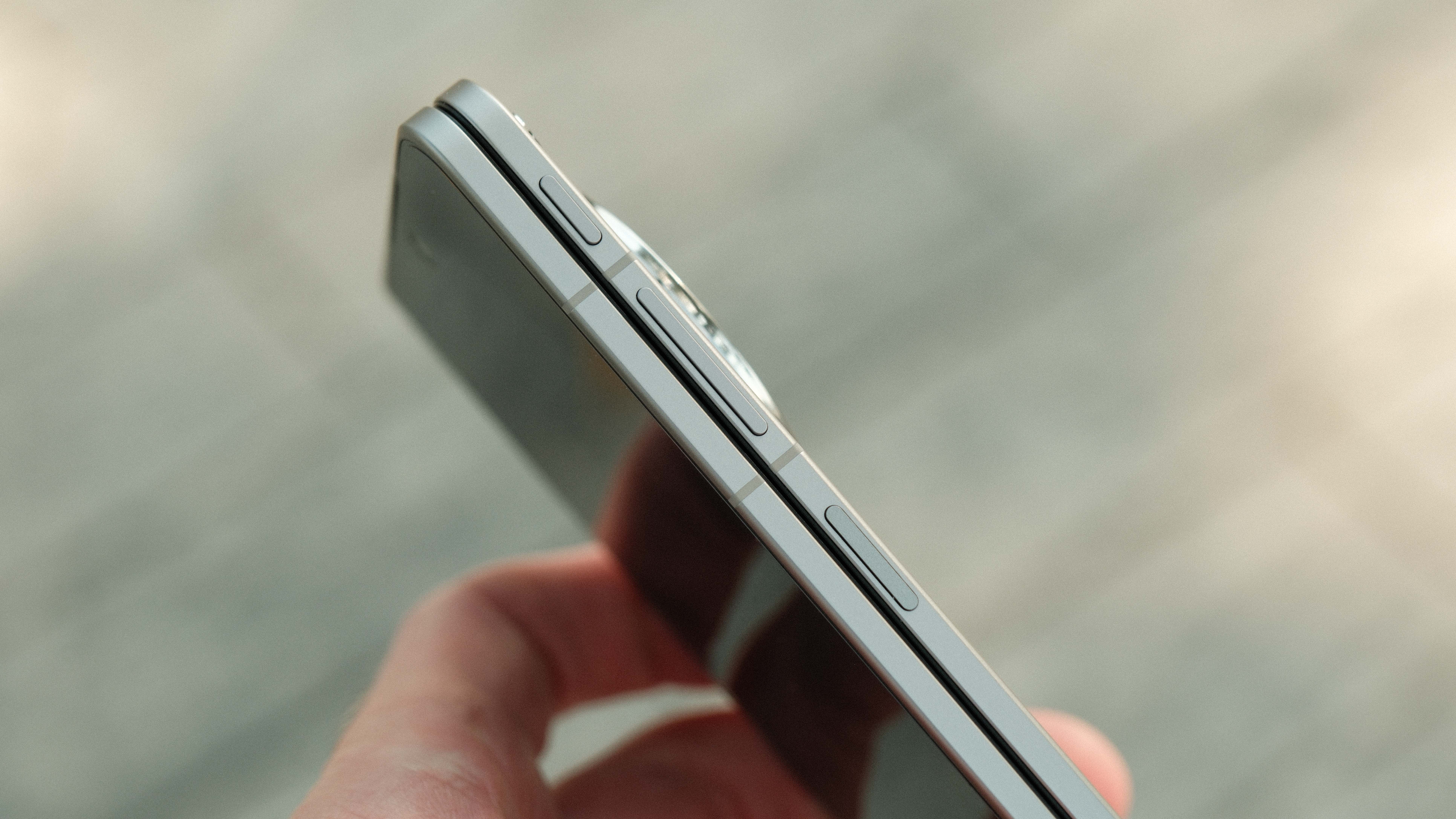 A side view of the device being held, showing the volume rocker and power button/fingerprint sensor. The phone is shown in its folded state, revealing its slim profile.