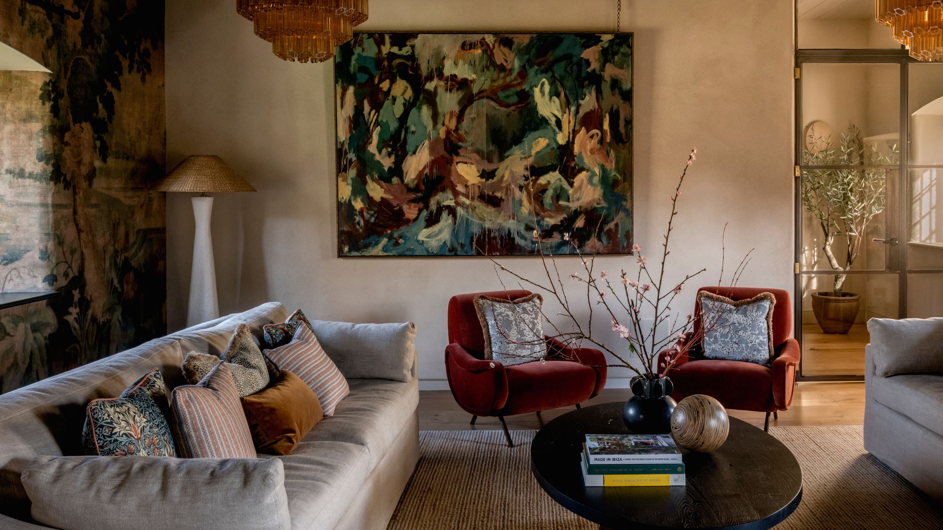 soft earthy living room with a botanical mural wall on the left, large abstract artwork and two neutral couches with burgundy armchairs