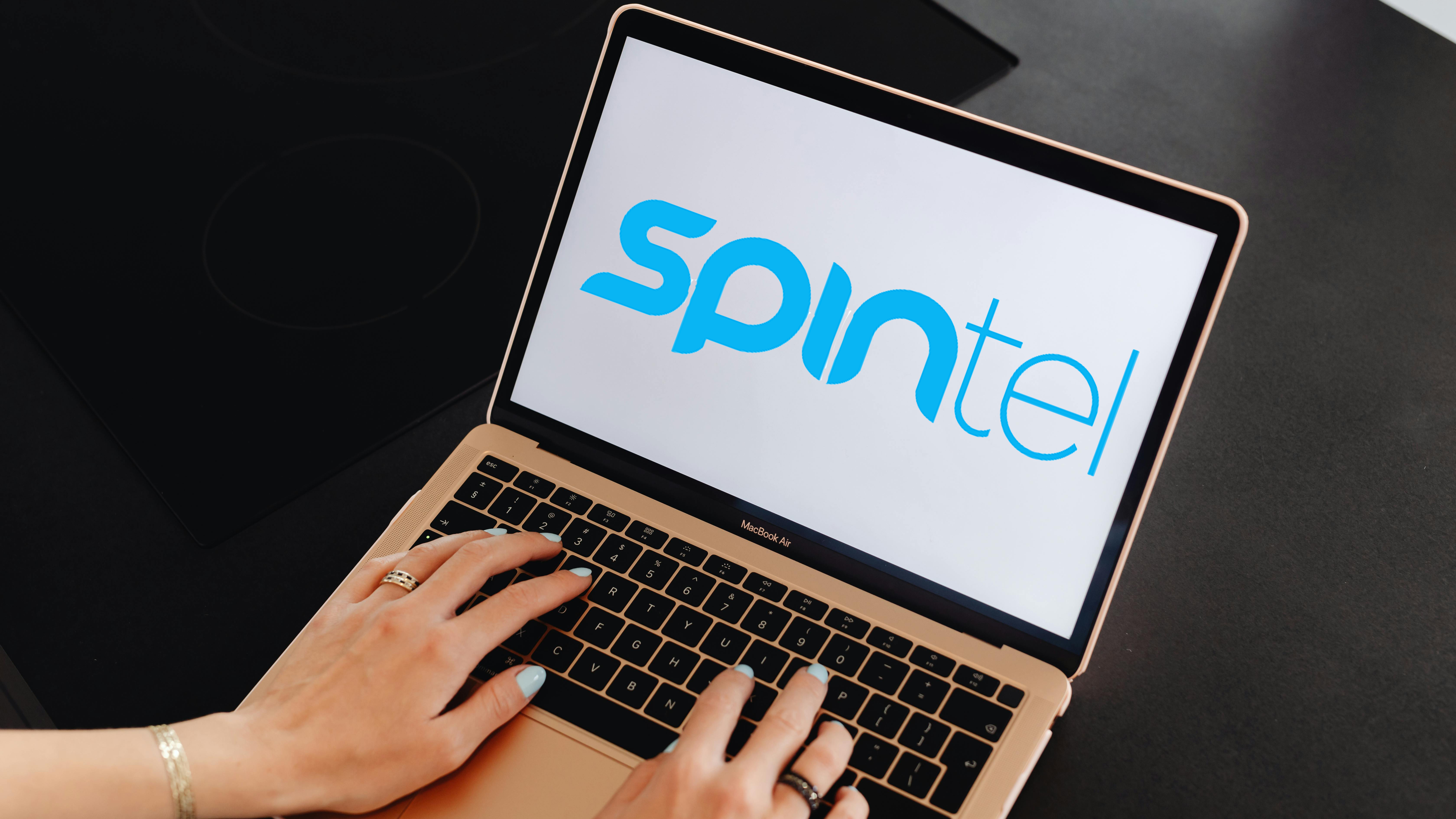 Hands typing on laptop with Spintel logo