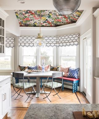 Light and airy dining area surrounded by windows with feature floral wallpaper on ceiling