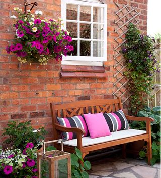 brick wall and window with wooden bench and cushions with pink hanging basket