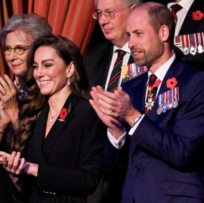 Kate Middleton wearing a black dress and Prince William wearing a blue suit and military medals clapping and smiling during the Festival of Remembrance concert