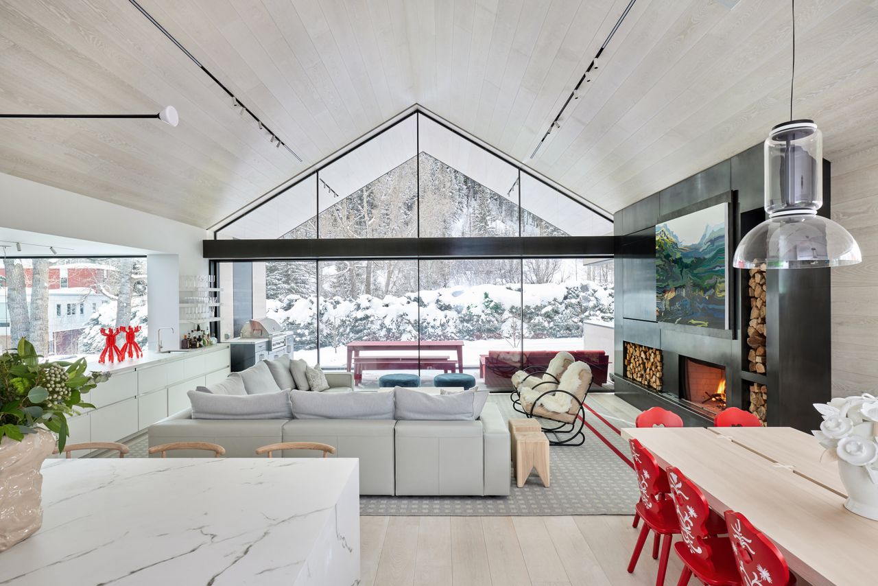 An open living room with a pitched roof and large windows overlooking a snowy outdoors.