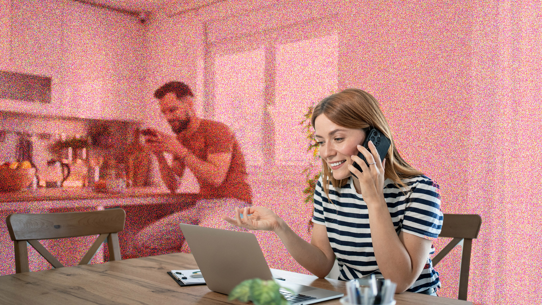 Young woman sitting at a kitchen table in front of a laptop, and talking on the phone