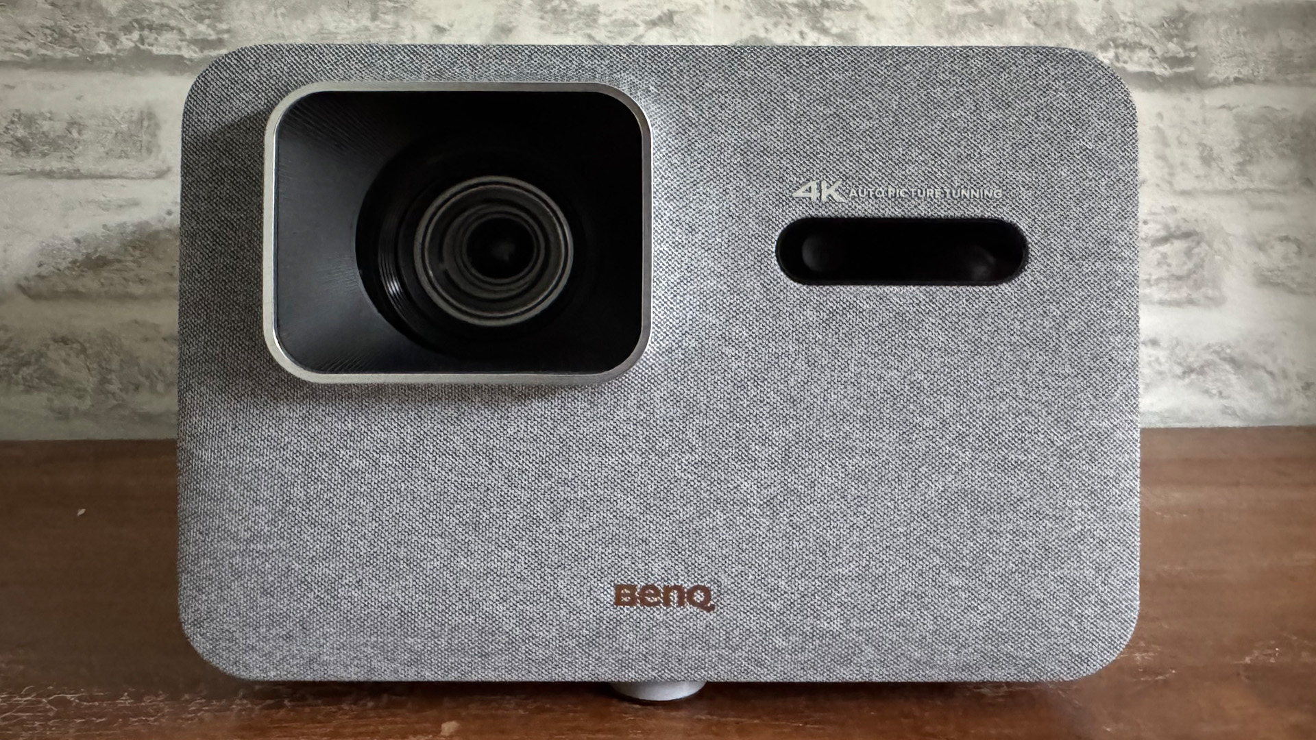 BenQ TK705i home cinema projector on wooden sideboard in front of white brick wall