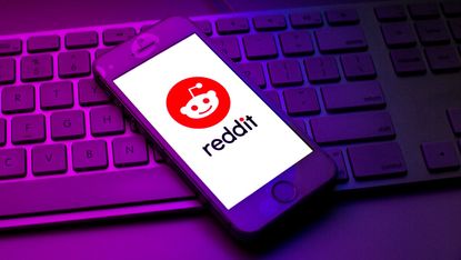 A Reddit logo is seen displayed on a smartphone on top of a computer keyboard