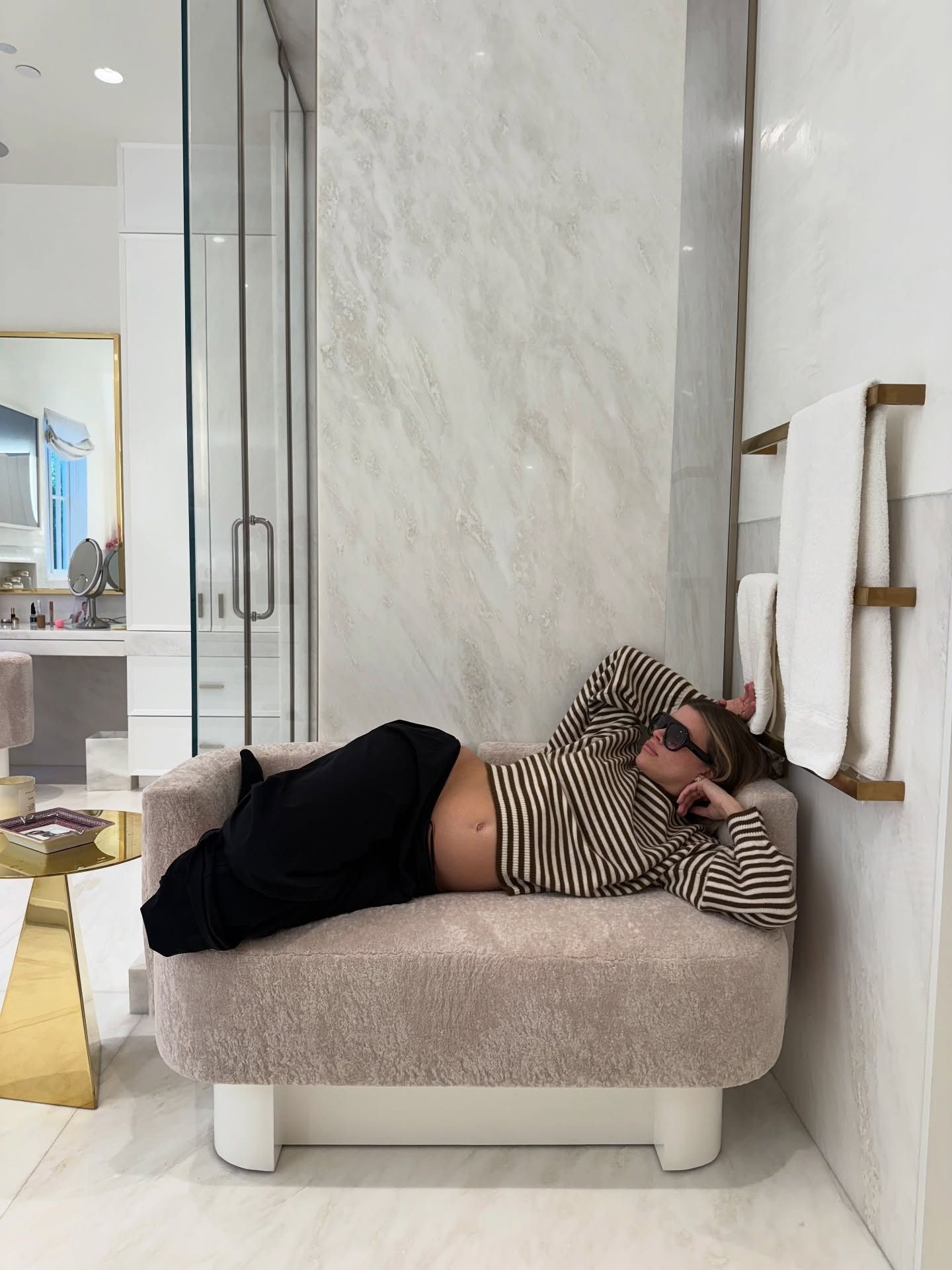 Sofia Richie Grainge lies on a sofa wearing a black and white striped knit with track pants and black sunglasses.
