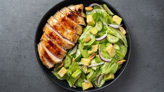 Grilled chicken sitting on a plate of salad