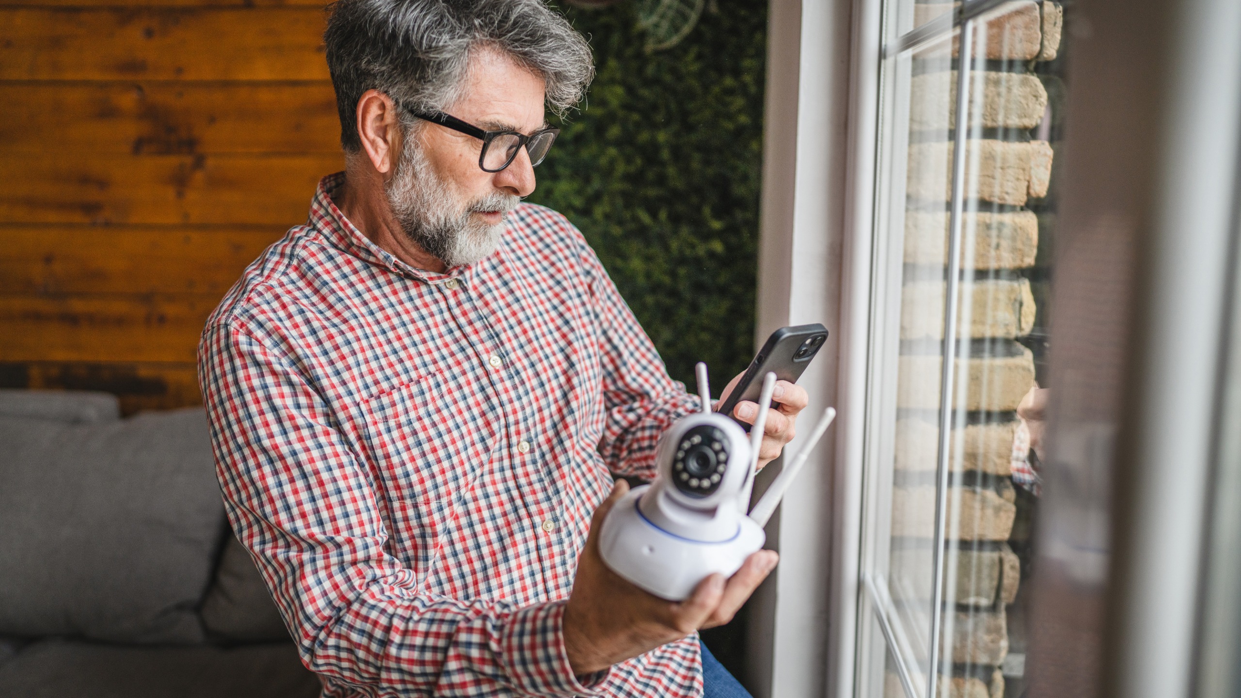 Man holding security camera, looking at smartphone