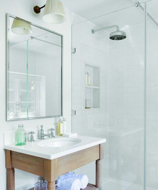 white bathroom with wooden washstand, rectangular mirror and glass shower enclosure
