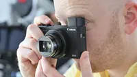 The Canon PowerShot G5 X Mark II being held up to someone's face with its pop-up viewfinder open