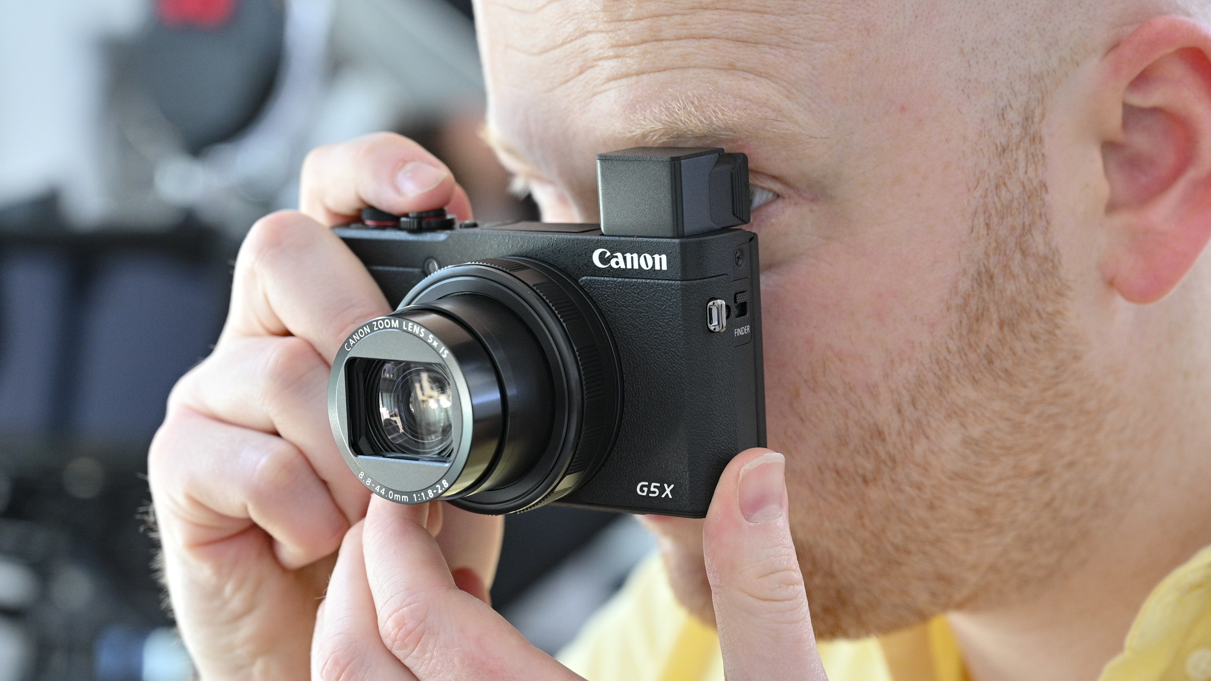 The Canon PowerShot G5 X Mark II, one of the best Canon cameras, being held up to someone's face with its pop-up viewfinder open
