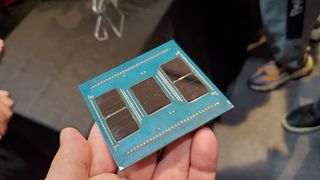 An AMD Zen 5 Turin-based EPYC processor with the head spreader removed, showing 13 chiplets, held in a hand