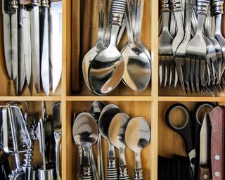 Interior of well-organized cutlery drawer with wooden drawer dividers separating out six types of silver cutlery
