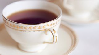 Black tea served in a white and gold bone china cup and saucer as suggested kitchen cleaning hack for cleaning glass