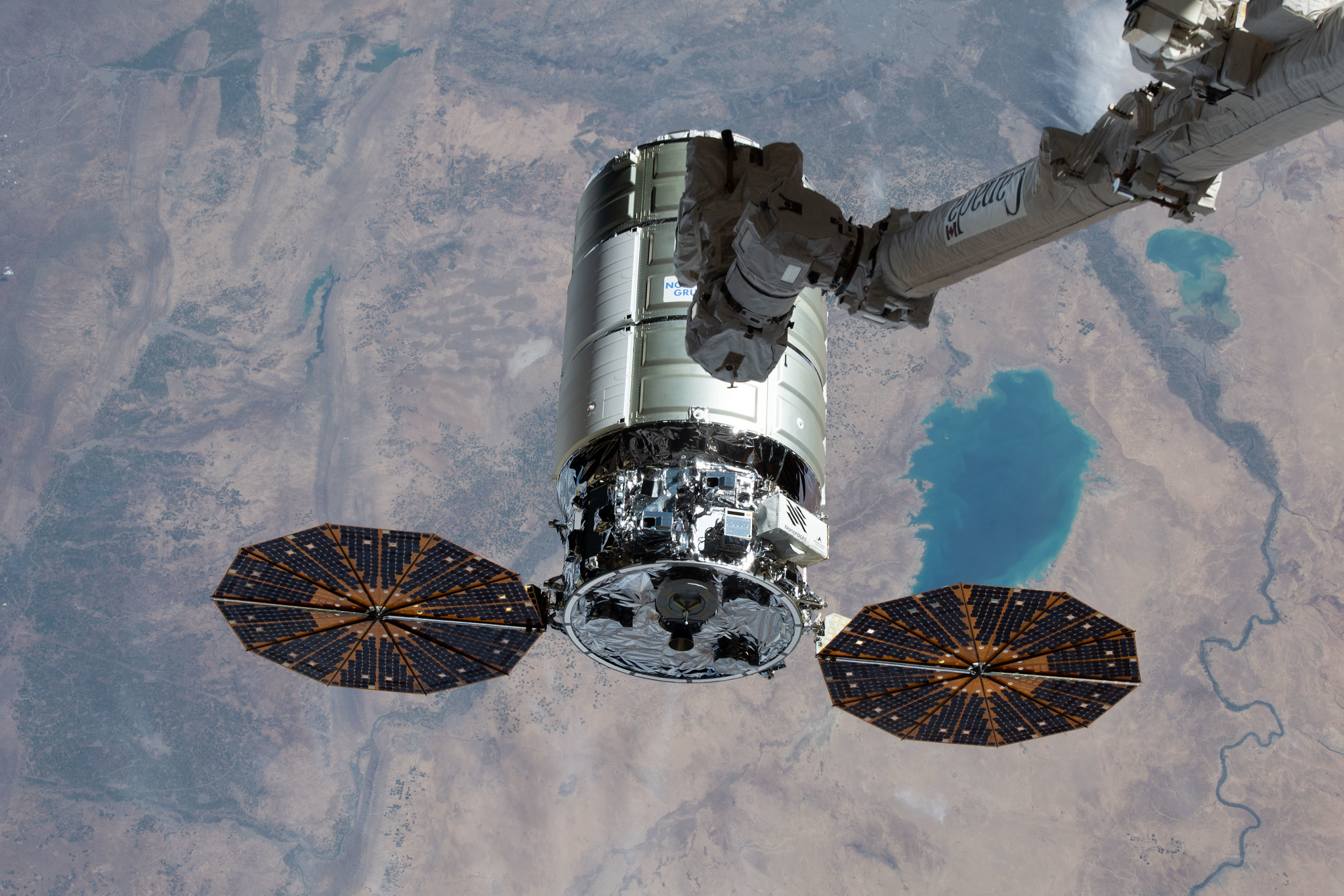 cygnus spacecraft with two solar panels with canadarm2 about to attach it at right