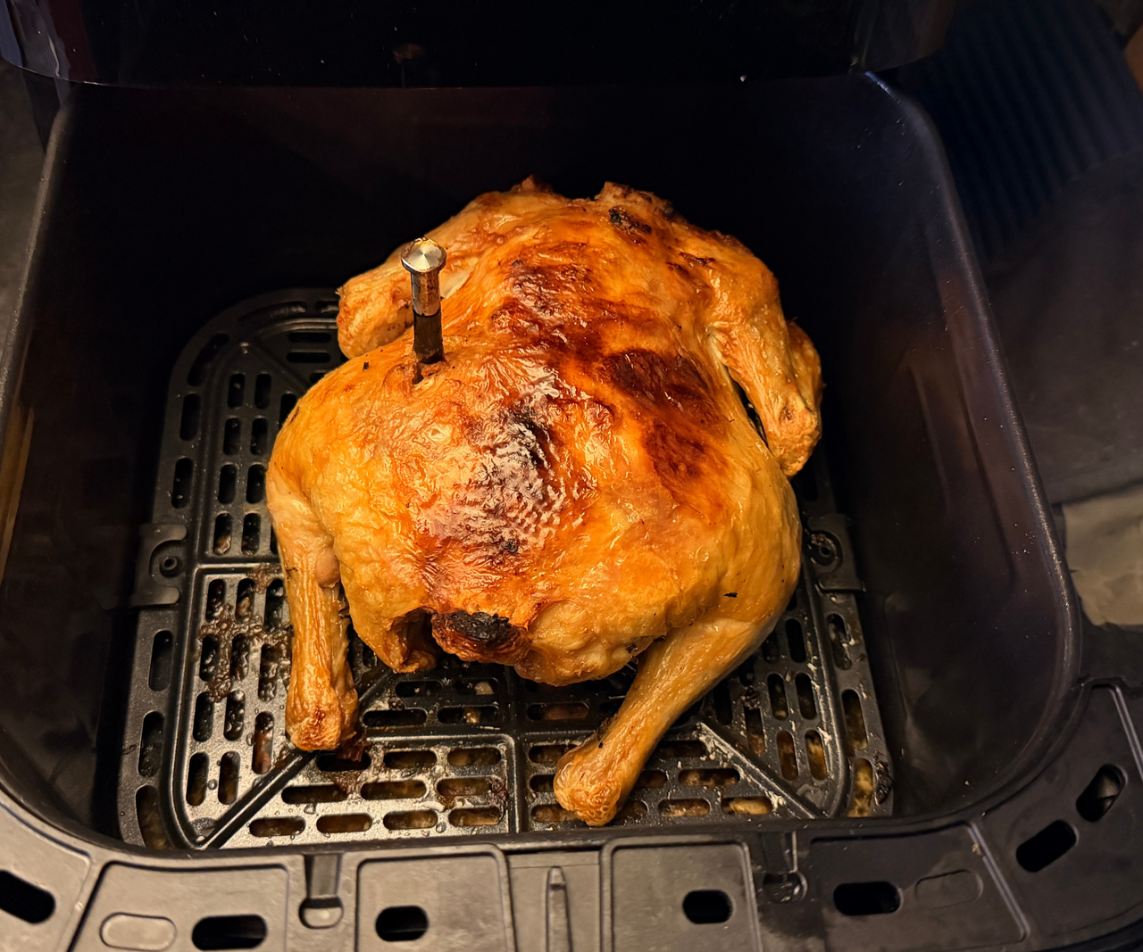 A whole roasted chicken inside a black square air fryer basket.