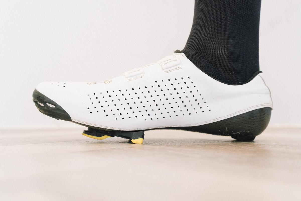 A close up of a white cycling shoe with a black socked foot in it