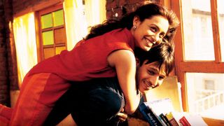 a woman in a red cress hugs a man in the style of a piggy back in an old apartment in a still from saathiya