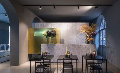 The interior of the restaurant is in gray tones with black tables and chairs, decorated with wildflowers.