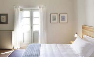 A light and airy room in the São Lourenço do Barrocal hotel. White walls with sketch art of nature on the walls. Wooden bed frame and white linen. To the fartherst wall, there is a balcony door which lets through a lot of light.