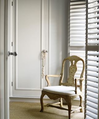 white bedroom with shutters, built in wardrobes and rococco armchair