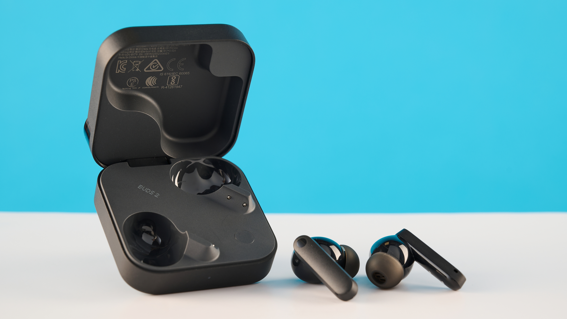 CMF Buds 2 in Dark Gray photographones on a gray table in front of a blue background