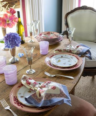 Wood table with with pink china plates, patterned napkins, pink glassware and champagne flutes