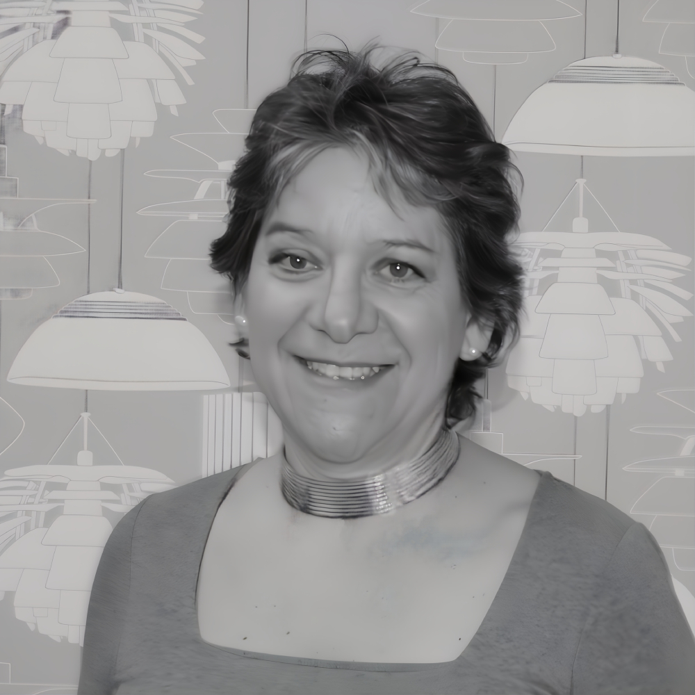 black and white image of female with short dark hair smiling at camera wearing grey top and detailed necklace