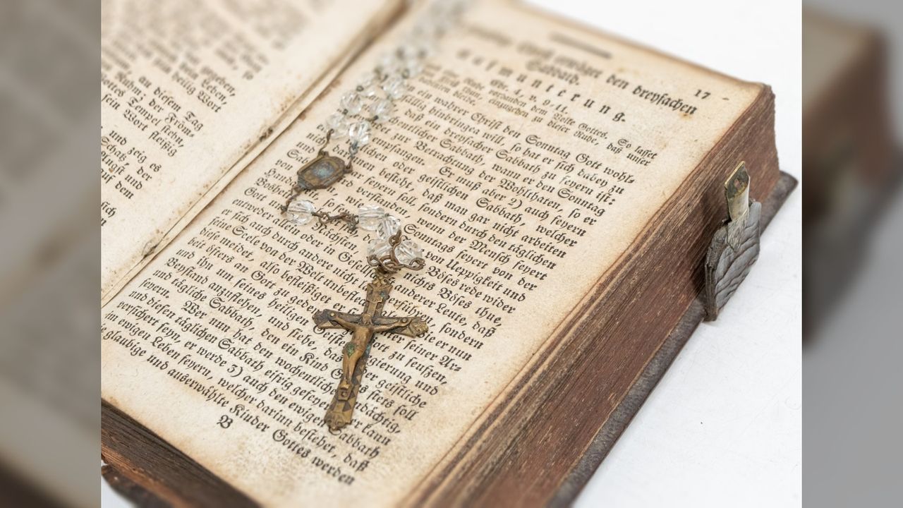 This image shows an old open bible with some clear rosary beads with a crucifix at the end draped across the page.