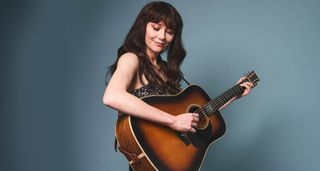 Molly Tuttle photographed with her custom Martin acoustic guitar against a blue-gray background.