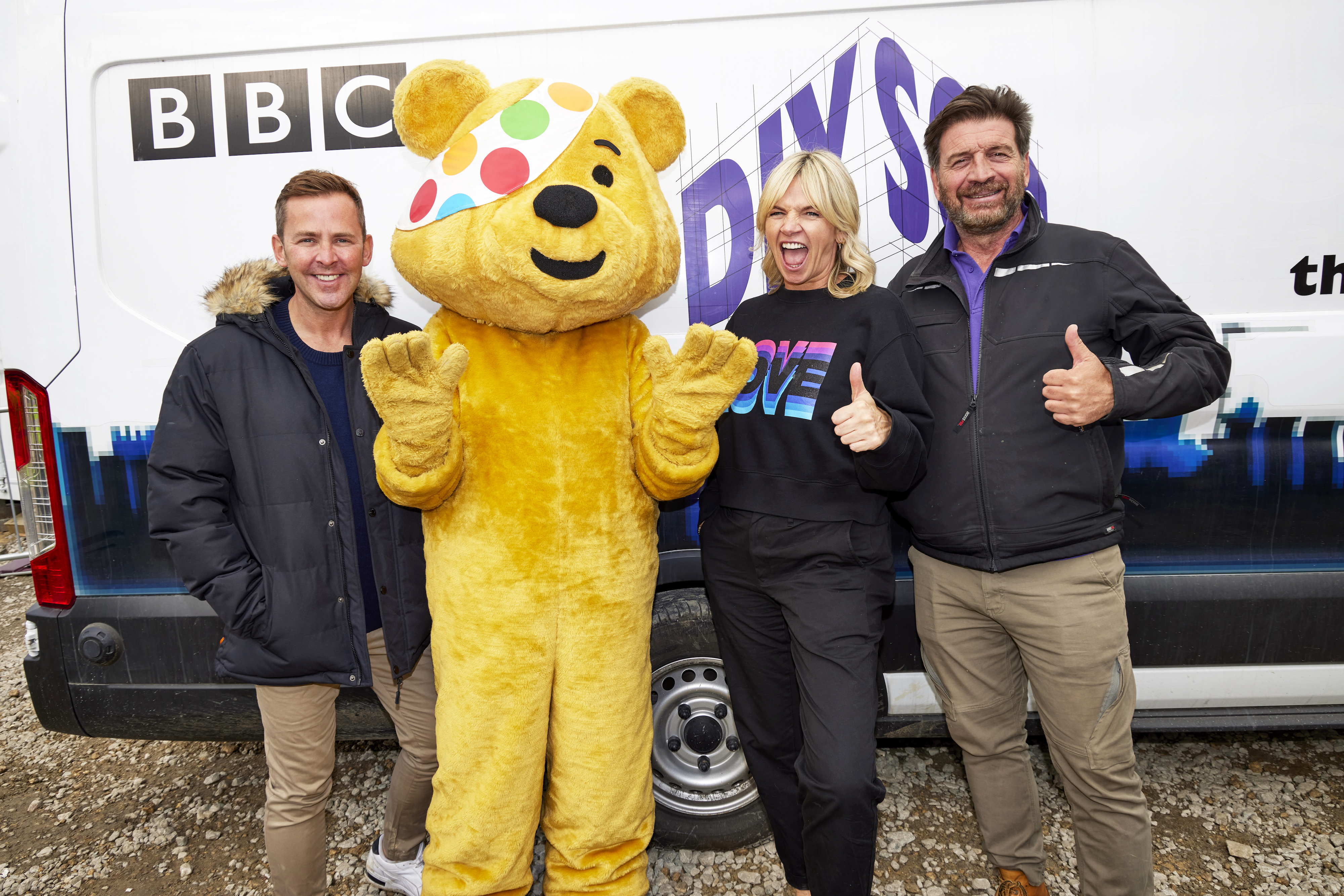 Scott Mills, Pudsey Bear, Zoe Ball and Nick Knowles give a thumbs up to the camera in front of a DIY SOS-branded van on the building site