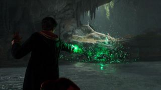 Hogwarts Legacy - A student wearing wizard robes casts a sparkling green spell while standing in a water-filled underground cave.