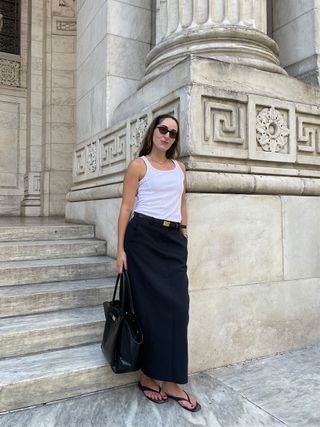 Anna LaPlaca wearing a white tank, black maxi skirt, H&M gold plate belt, Demellier New York Tote, and A.Emery Kinto Sandals