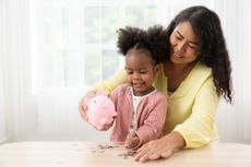Mom and young daughter putting coins in a pink piggy bank