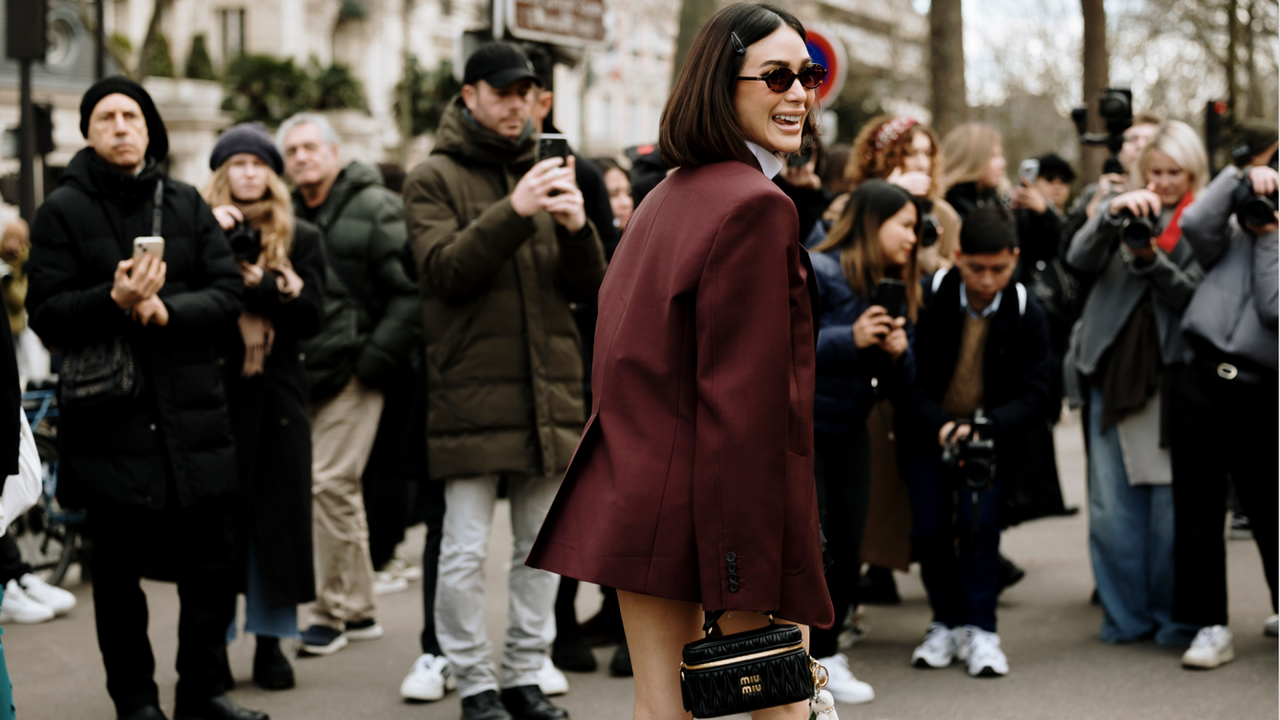 a guest attends the Paris fall 2024 fashion week shows wearing oversized dark red blazer, sunglasses, and black miu miu bag 