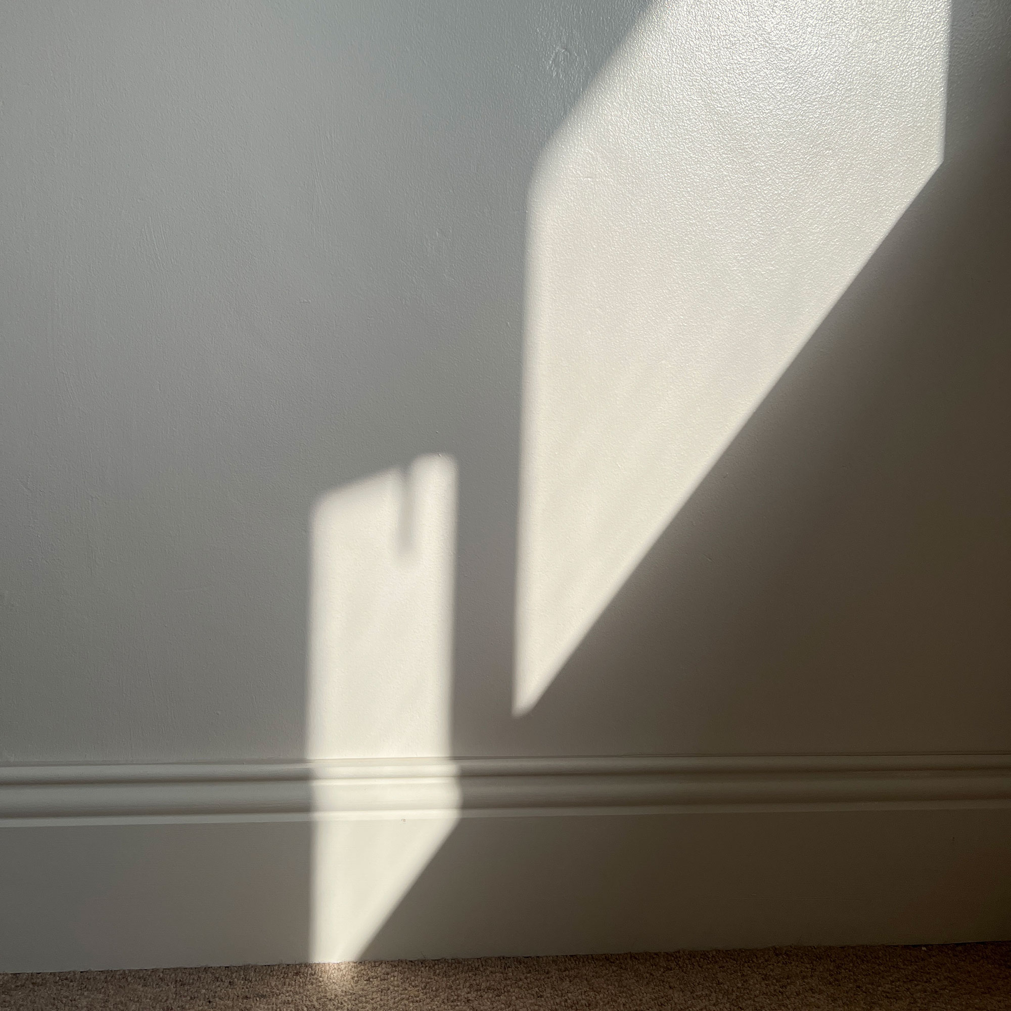 Sunlight cast onto white wall and skirting board