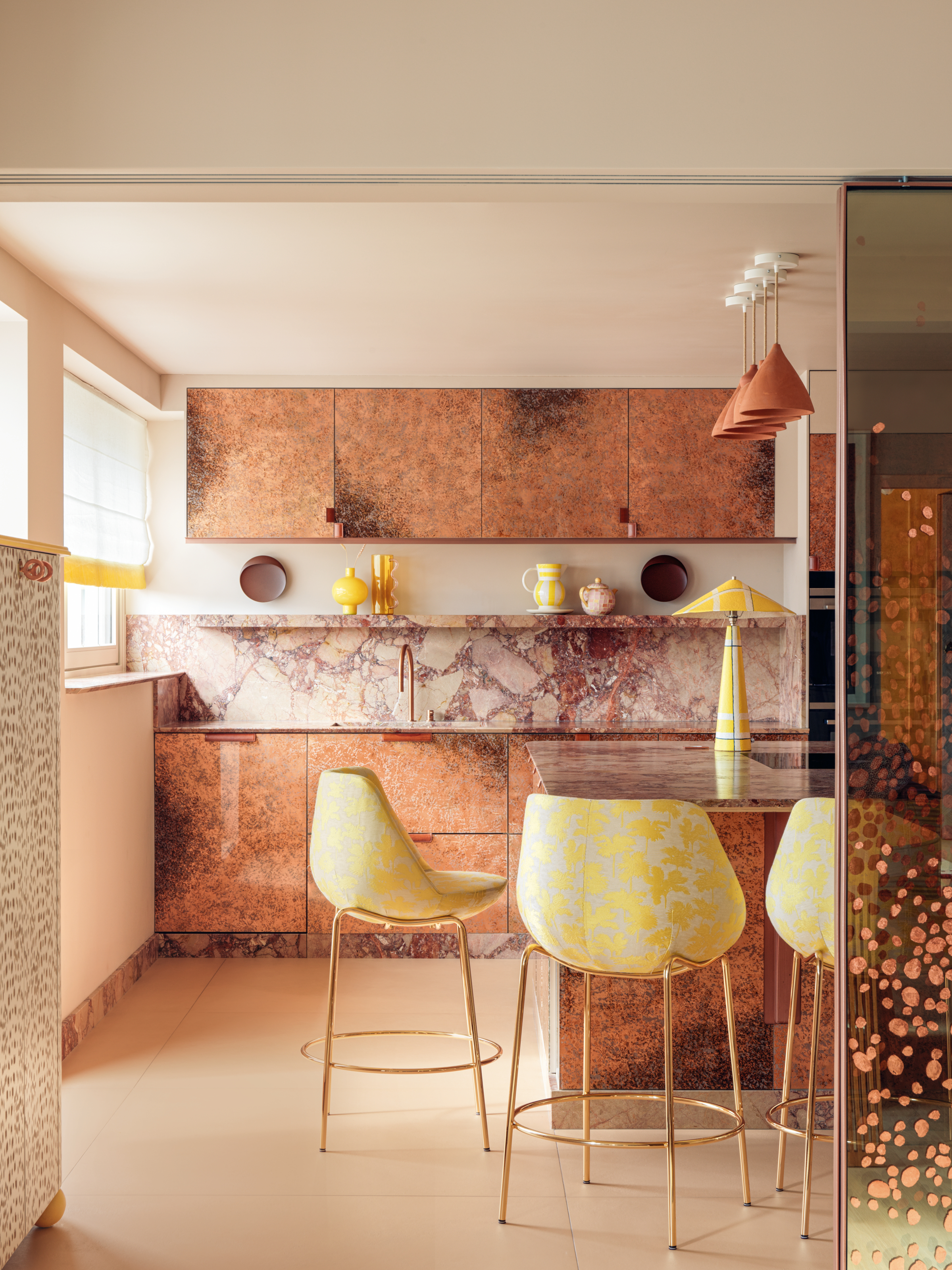 Copper kitchen with pink marble splashback and pale yellow bar stools