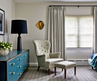 bedroom with blue chest and white armchair and footstool