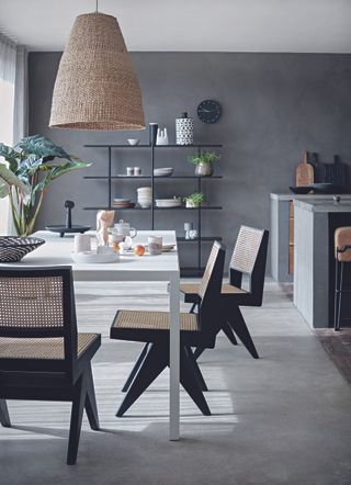 Dining area with grey table, cane chairs, dark grey walls and large rattan lampshade